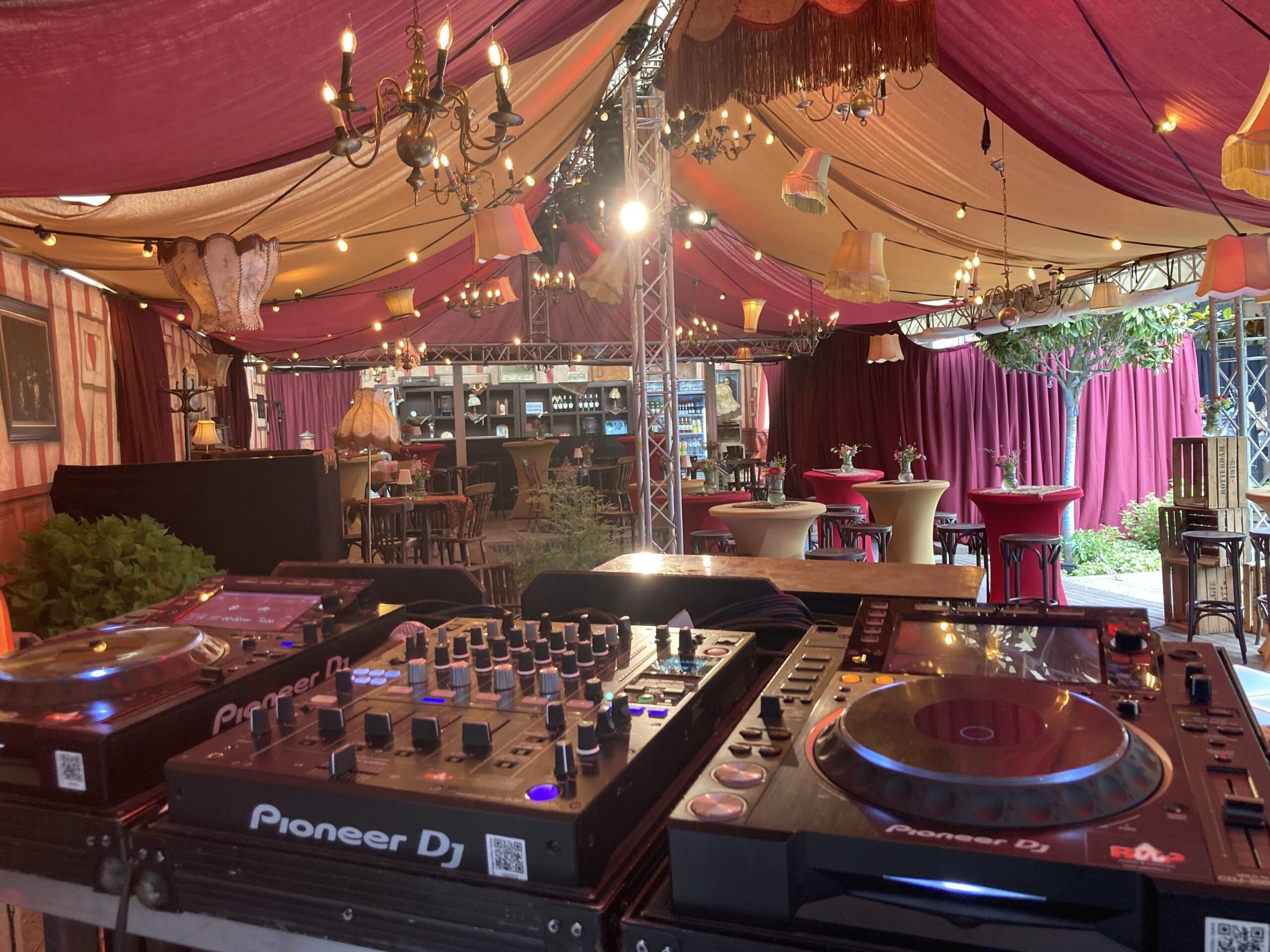 Dj-set in een tent met kroonluchters en statafels op de achtergrond