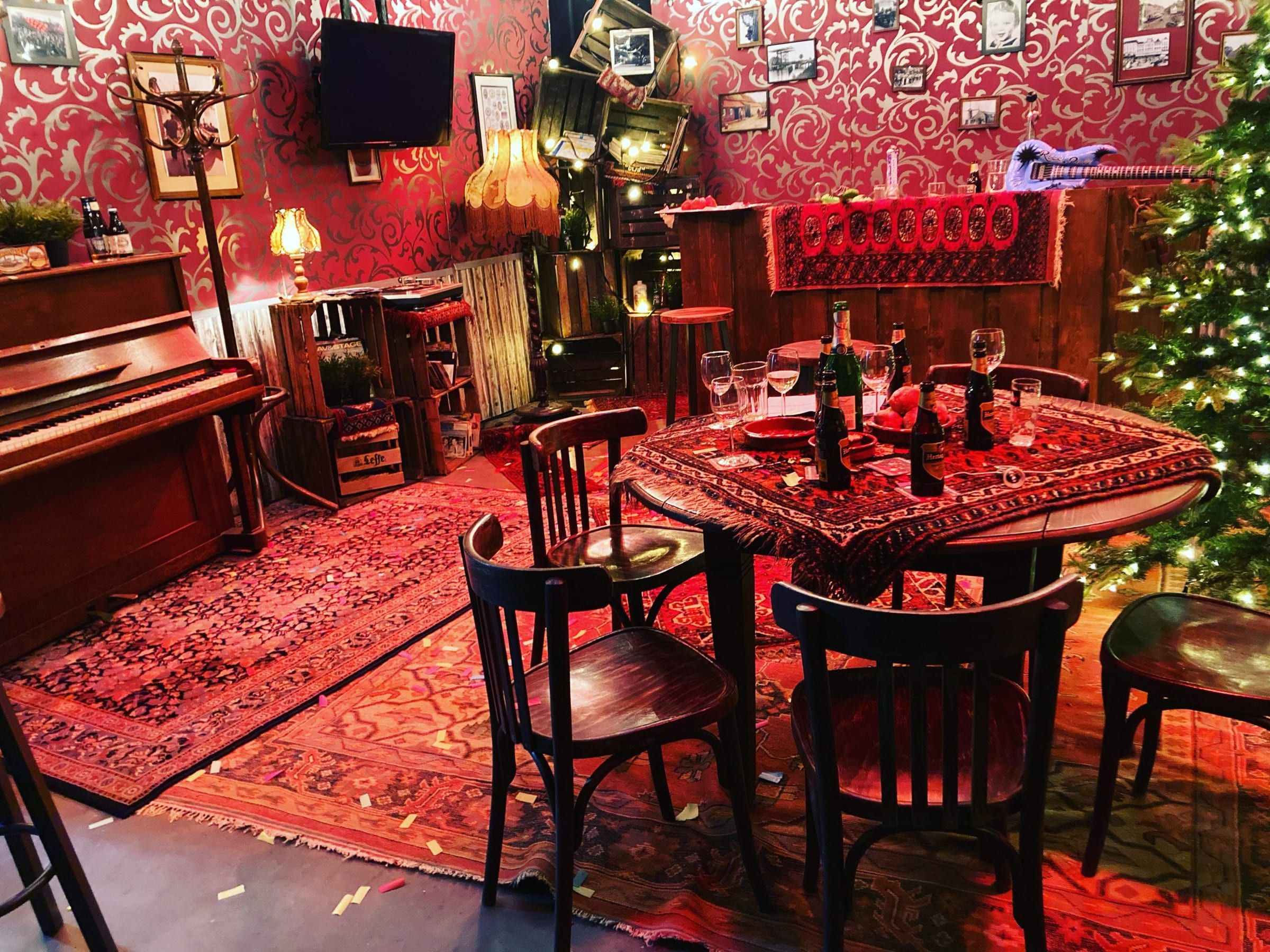 Kroeghoek met piano, cafétafel, Perzisch tapijt en schemerlampen