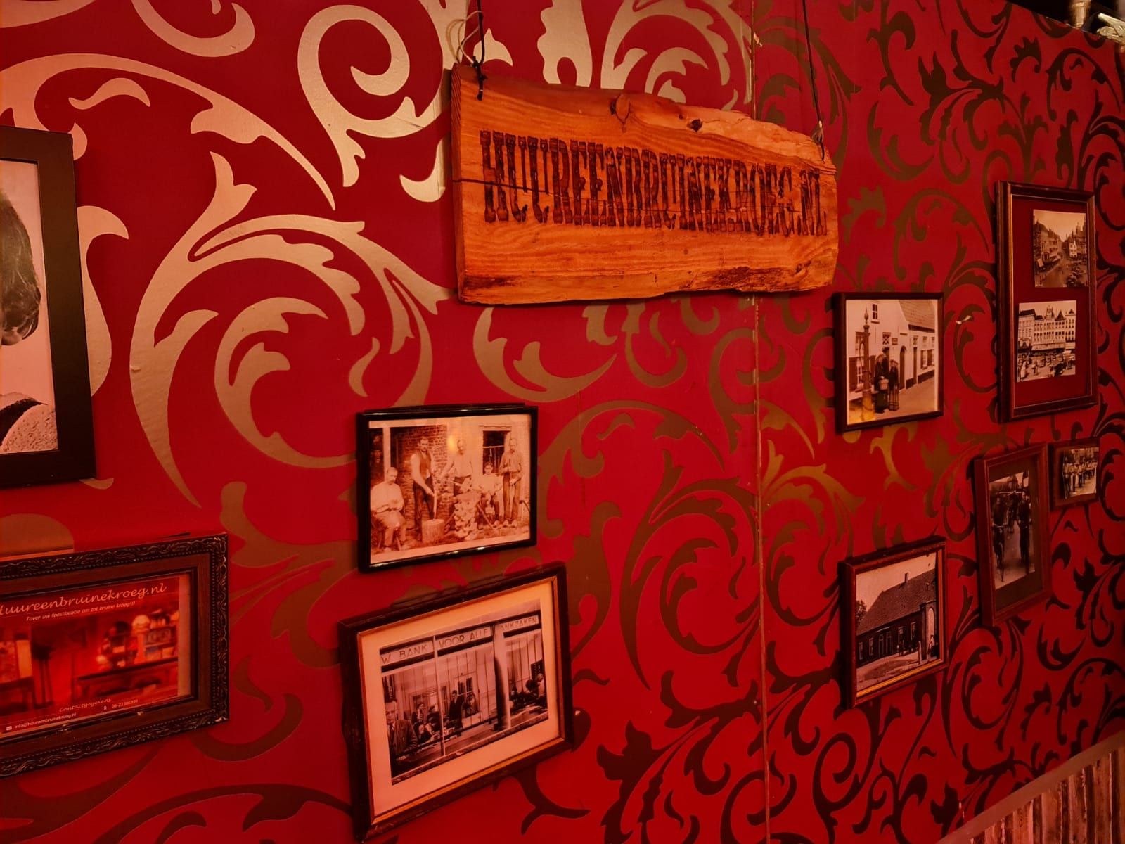 Rode kroegwand met oude foto's in lijstjes en een houten naambord