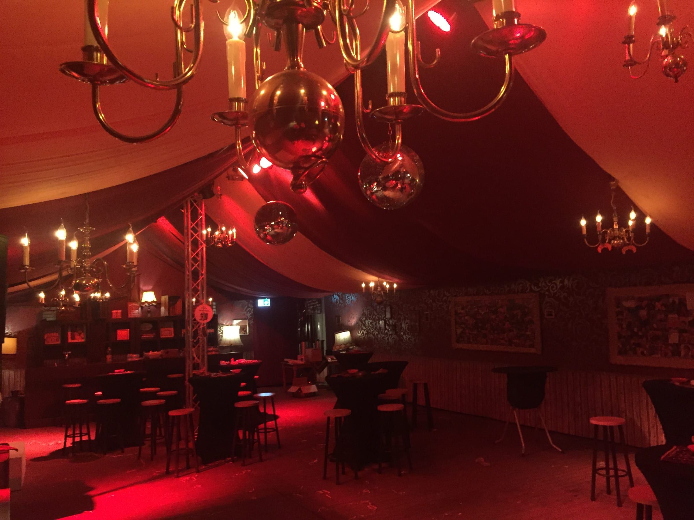 Kroonluchters en spiegelbollen boven statafels in een verlichte tent
