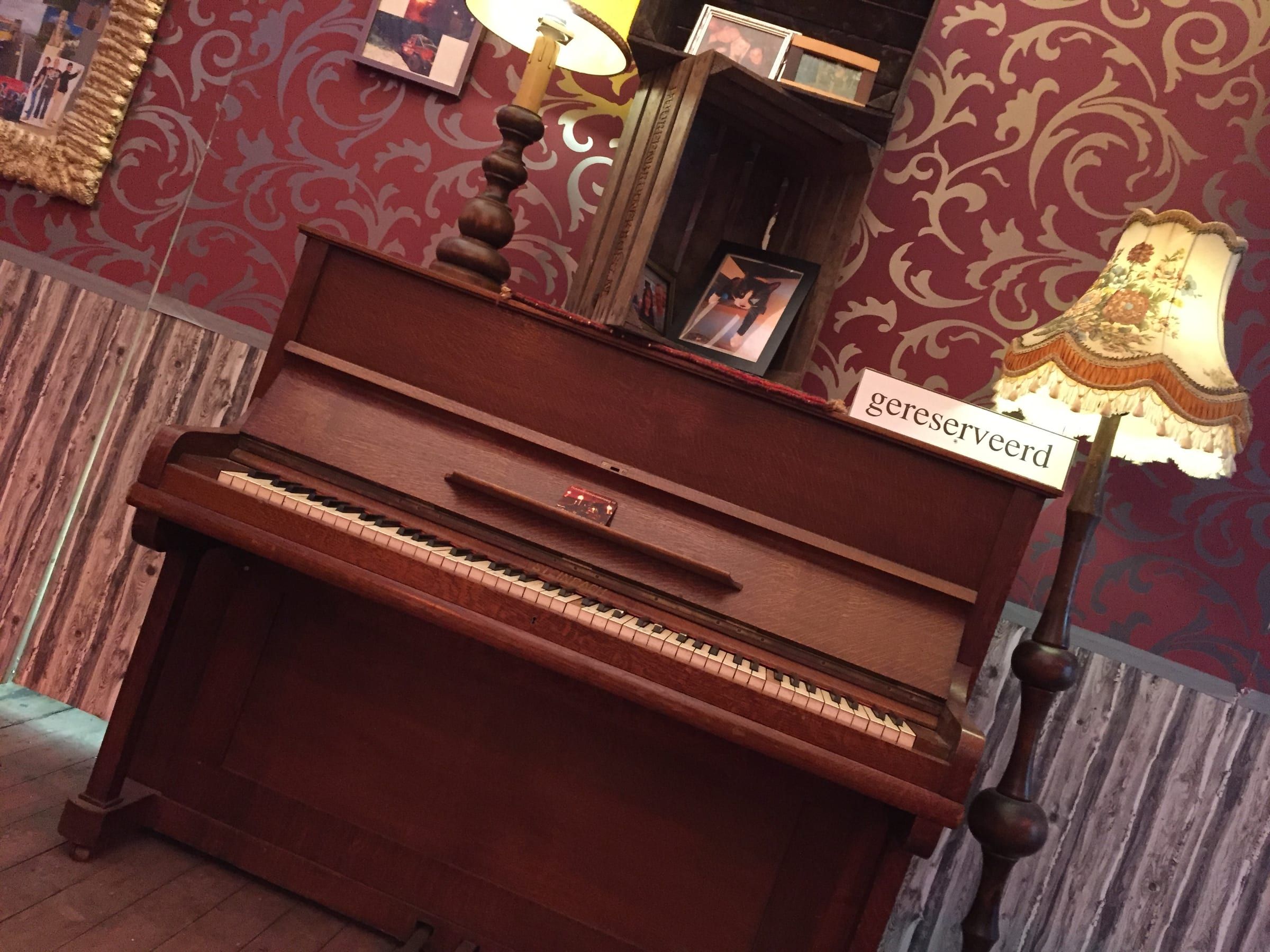 Oude piano met schemerlamp en een bordje gereserveerd voor rood krullenbehang