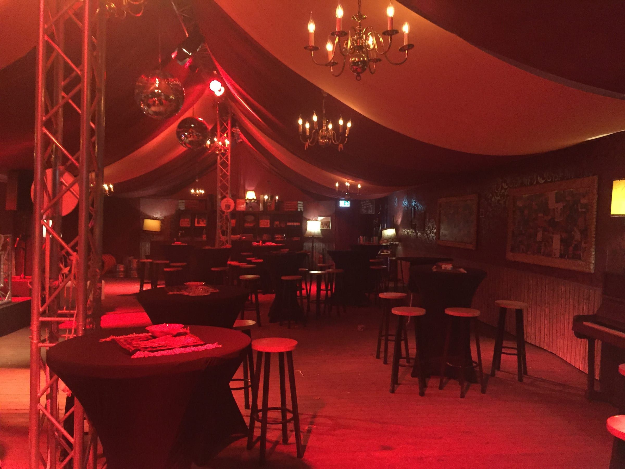 Overzicht van een opgebouwde bruine kroeg in een tent, in warm rood licht