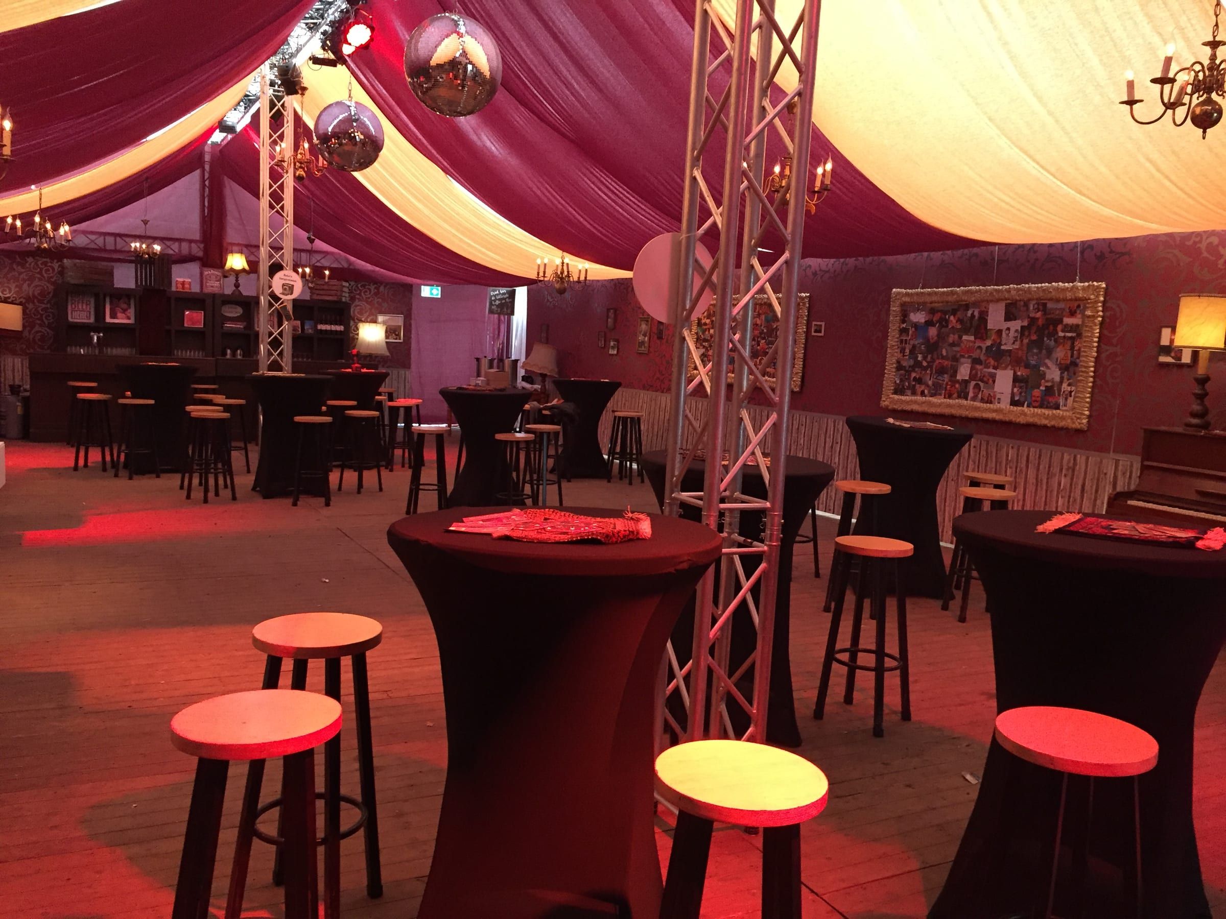 Bruine kroeg in een tent met rood doek, statafels, barkrukken en kroonluchters aan truss
